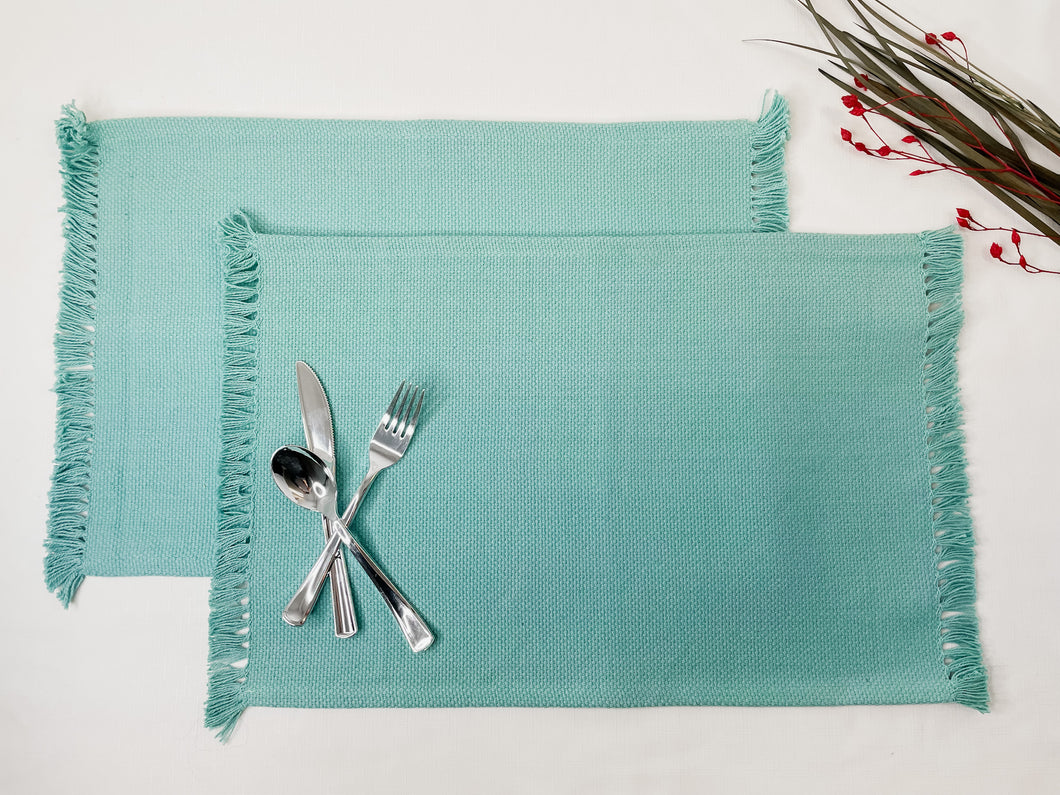 two 100 % cotton coral placemat with fringes on the end stack together with cutlery on the left corner and some faux leaf on the right upper corner for design
